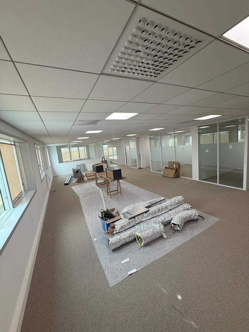 Plateau de bureaux en travaux : gaines souples posées au sol sur une bâche, diffuseur de soufflage dans le faux plafond.