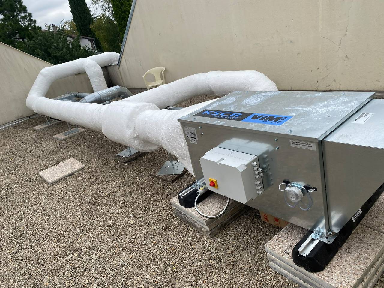 Centrale de traitement d'air installée en toiture sur plots antivibratiles, raccordée à des conduits souples calorifugés.