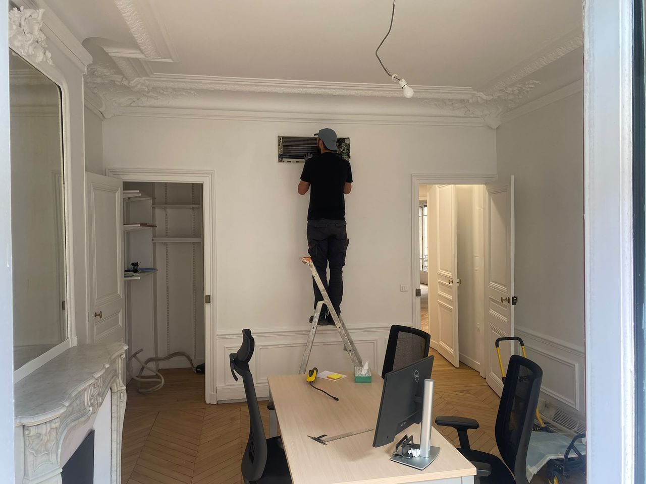 Technicien Paris Génie Clim installant une unité intérieure au plafond d'un appartement haussmannien, moulures, cheminée de marbre et parquet en point de Hongrie.