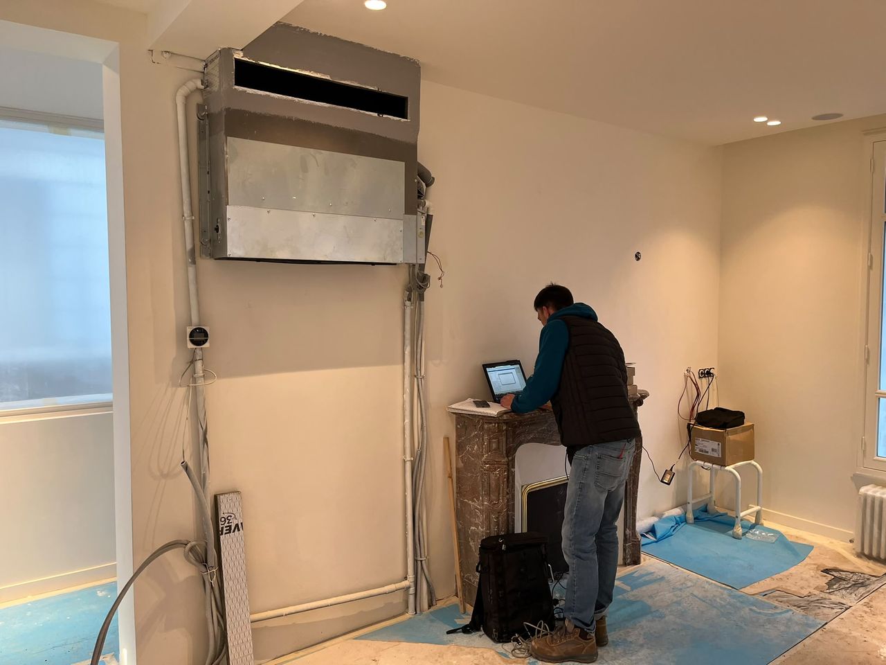 Technicien Paris Génie Clim effectuant les réglages de mise en service sur un ordinateur portable, sous une unité gainable fixée en hauteur.