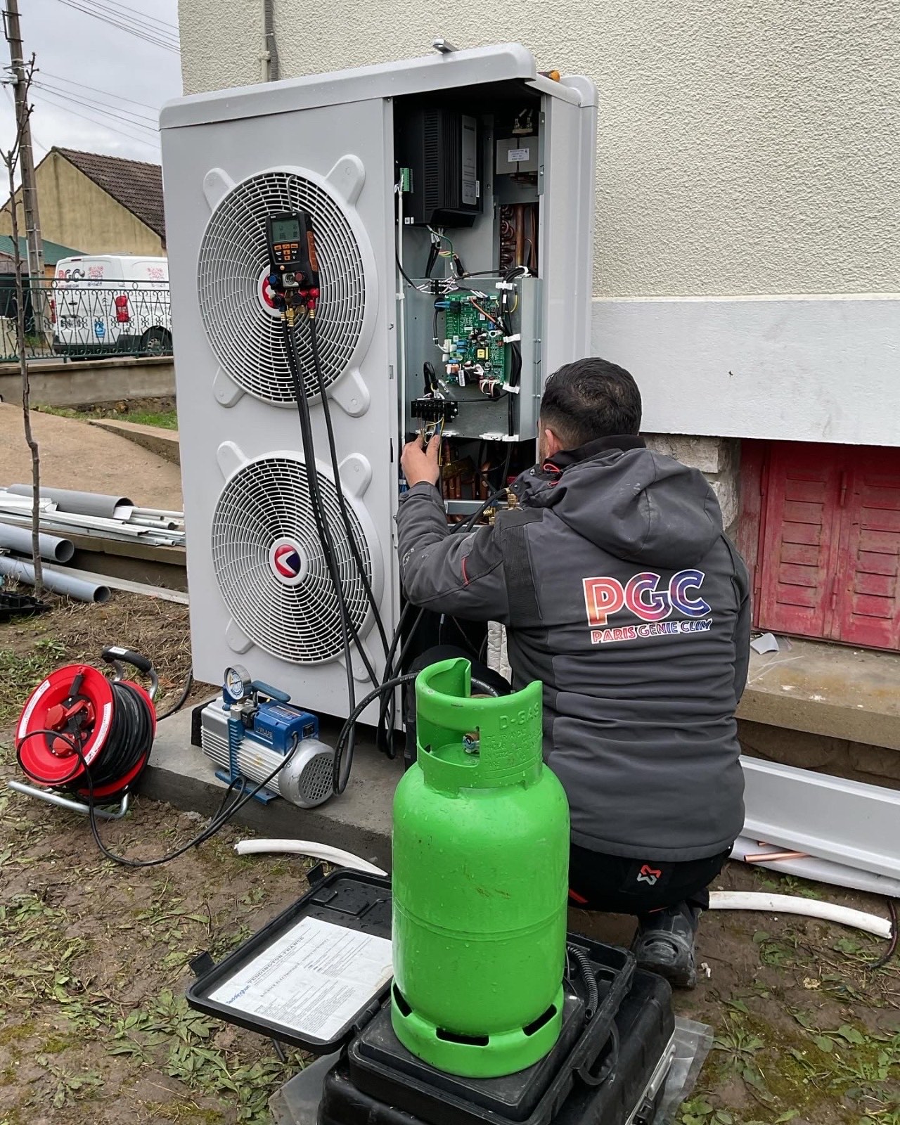 Technicien Paris Génie Clim réalisant un tirage au vide sur un groupe extérieur, pompe à vide et bouteille de fluide frigorigène posées au sol, camionnette PGC en arrière-plan.